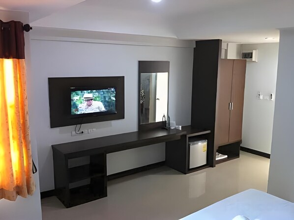 A modern hotel room with a flat-screen TV mounted on the wall, a built-in vanity with a mirror, a dark wooden wardrobe, and a small bedside table. - S K Airport (Chiang Mai)
