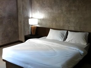 A hotel room with a large bed, a nightstand with a lamp, and a plain wall. - S K Airport (Chiang Mai)