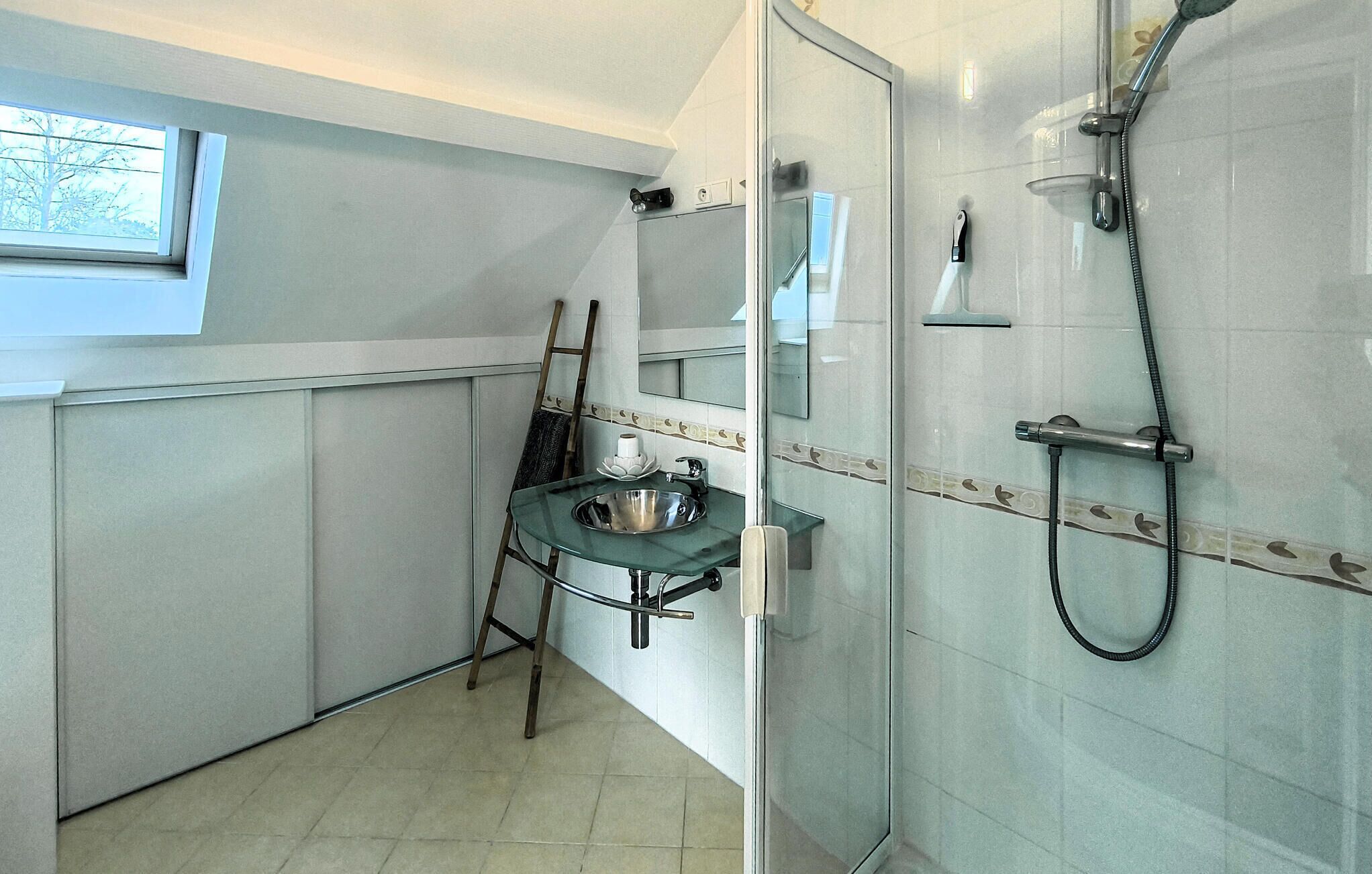 A bathroom with a glass shower enclosure, a sink with a bowl, and a ladder leaning against the wall.