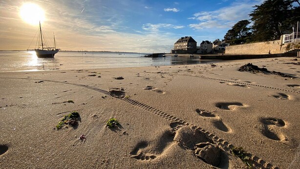 A beach with footprints, a sailboat, and buildings in the background. - Cozy apartment in Larmor-plage with WiFi (Larmor-plage)