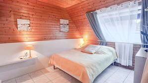 A bedroom with a wooden ceiling, a bed with a white mattress, a nightstand with a lamp, and a window with sheer curtains. - Cozy apartment in Larmor-plage with WiFi (Larmor-plage)
