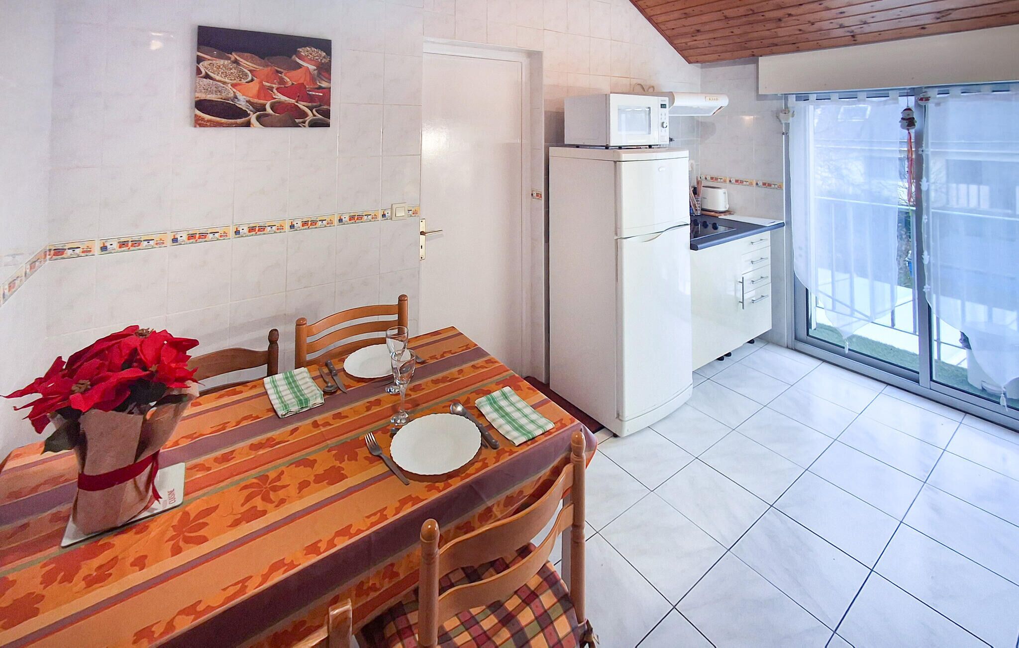 A dining area with a table set for four, a refrigerator, a microwave, and a view of the outside through a glass door.