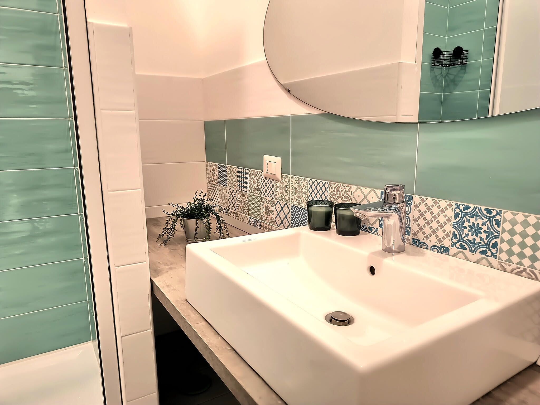 A bathroom with a white sink, a mirror, and a patterned tile backsplash.