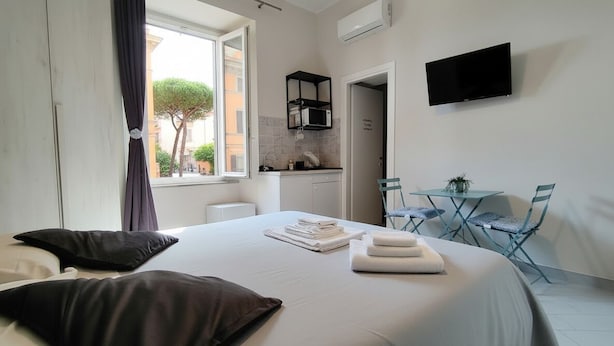 A hotel room with a bed, a desk, a chair, a TV, and a window with curtains. - Pansini Ruggiero's Apartaments (Naples)