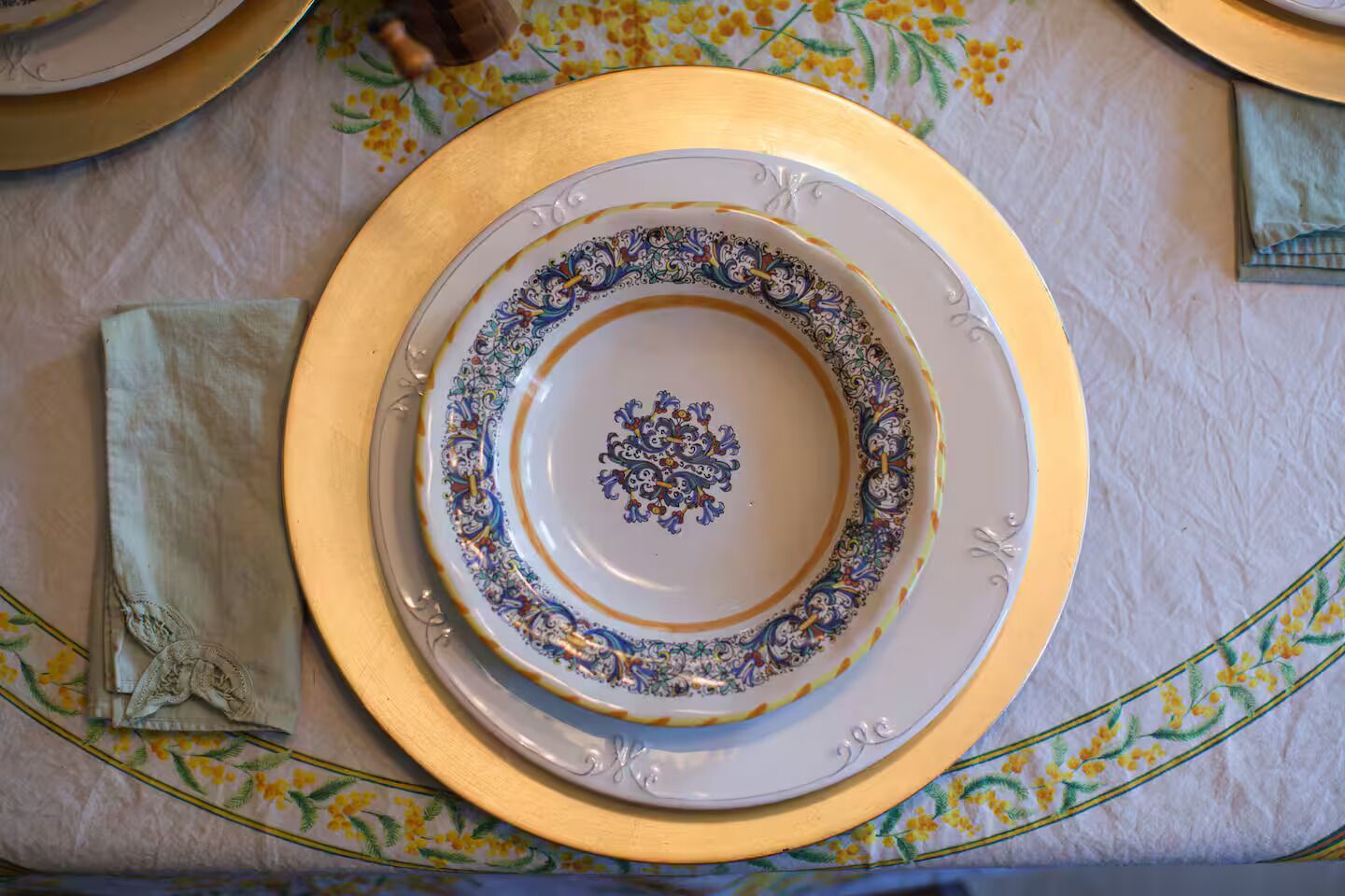 Una mesa con un plato blanco, un plato con borde dorado y una servilleta.