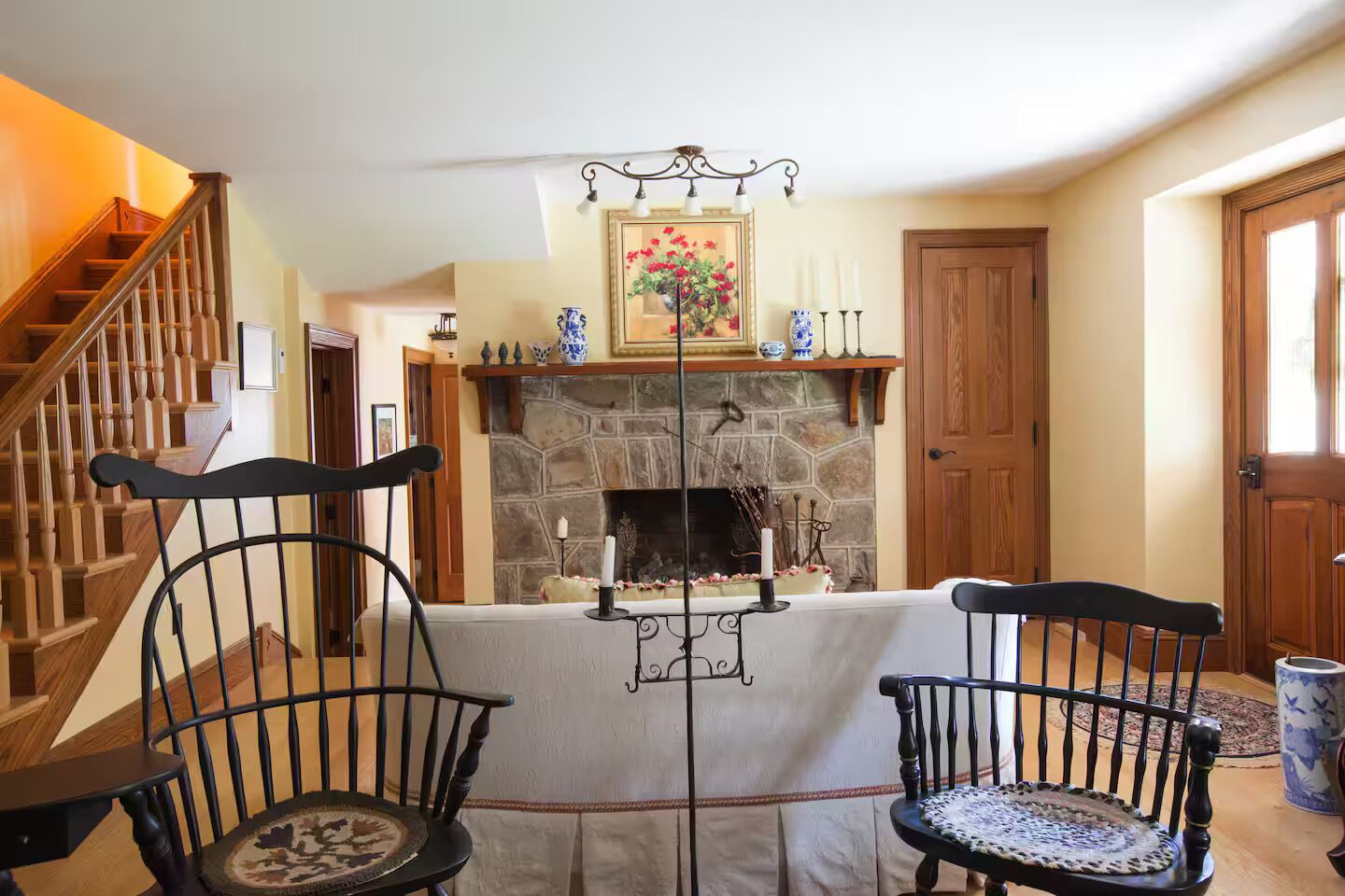 Un salón acogedor con chimenea, escalera de madera y dos sillones negros con asientos de mimbre.