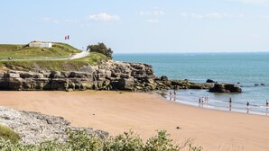 Un paysage côtier avec une plage de sable, des falaises rocheuses et une colline herbeuse sur laquelle se trouvent un bâtiment et un drapeau.