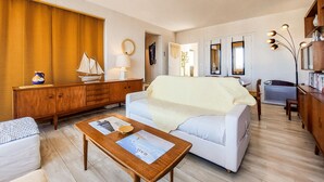 Un salon comprenant un canapé, une table basse, un meuble en bois et une fenêtre avec des stores.