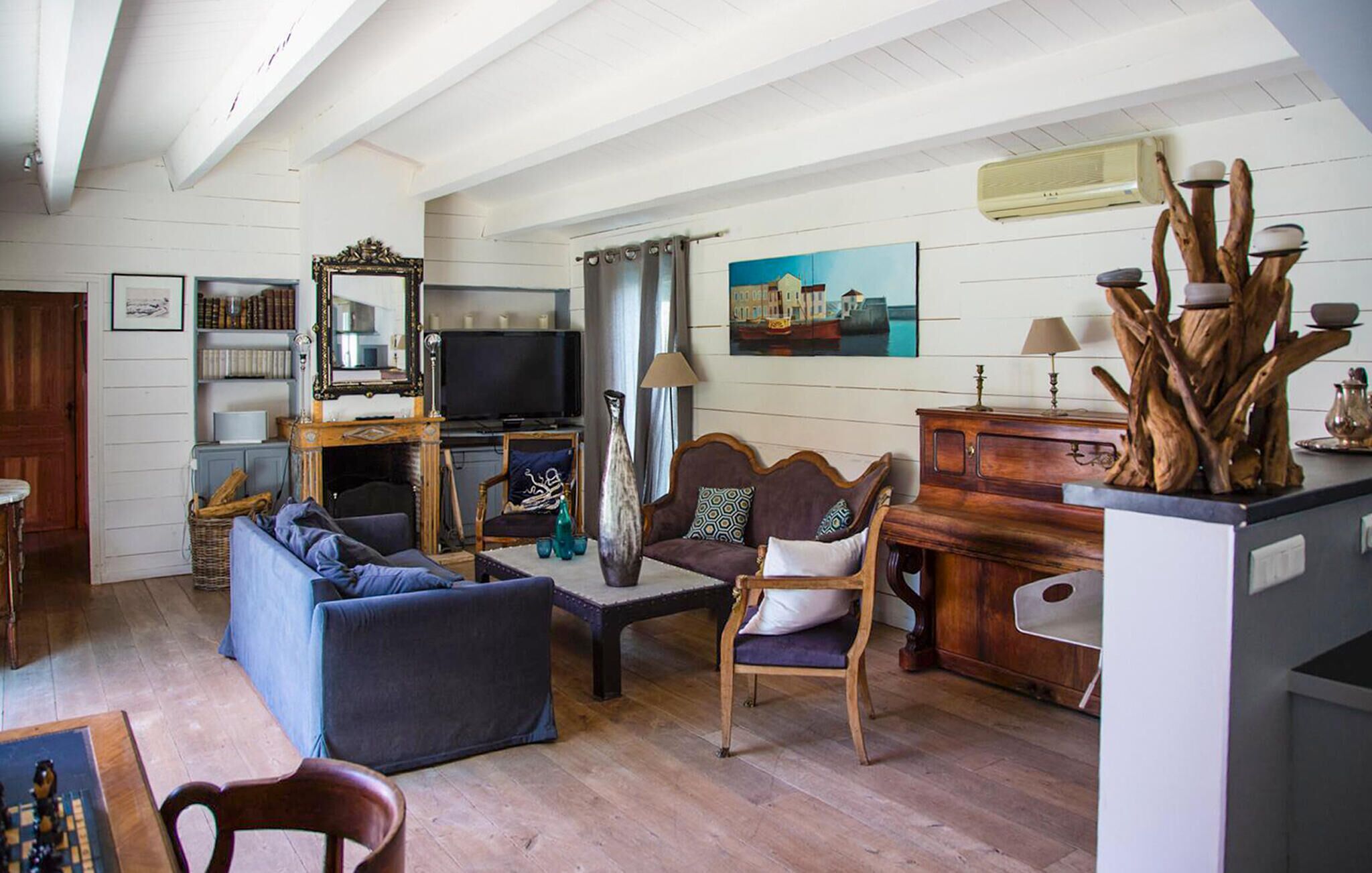 Een gezellige woonkamer met een bank, fauteuil en een televisie. Er is een boekenkast, een lamp en een schilderij aan de muur.