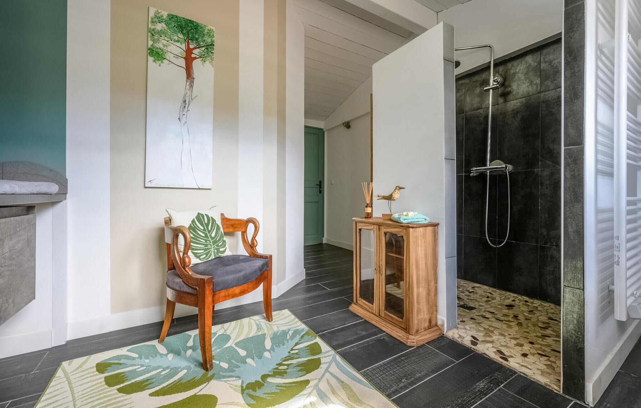 Un baño moderno con ducha, una silla de madera, un mueble pequeño y un cuadro grande en la pared.