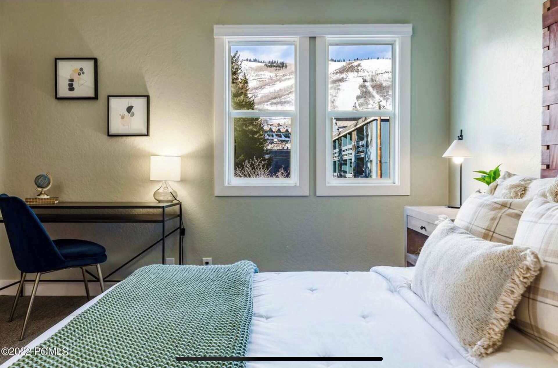 Un dormitorio con cama, escritorio, silla y ventana con vista a un paisaje nevado.