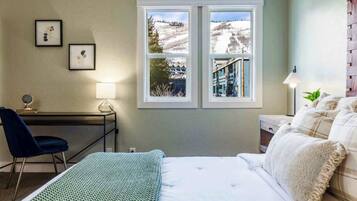 Un dormitorio con cama, escritorio, silla y ventana con vista a un paisaje nevado.