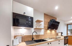 Une cuisine moderne dotée d’un four à micro-ondes encastré, d’un robinet noir et de meubles de rangement en bois.