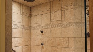 Zona de ducha con paredes de azulejos, un taburete de madera y un pasamanos.