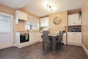 A modern kitchen with white cabinetry, a dining table with chairs, a clock on the wall, and a microwave on the countertop.