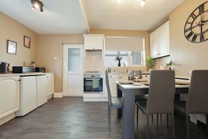 A modern kitchen with white cabinetry, a dining area with a table and chairs, and a large wall clock.