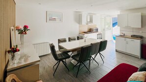 A modern kitchen with white cabinets, a dining area with a white table and black chairs, and a red sofa in the foreground. - Stunning home in Coutances with private swimming pool, can be inside or outside (Coutances)
