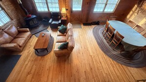 Een knus chaletinterieur met een houten vloer, leren bank, een ronde eettafel en een open haard.