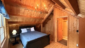 Een slaapkamer met houten vloer, een bed, nachtkastje, lamp en een houten deur.