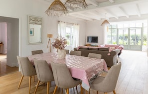 Un coin repas avec une table dressée pour six personnes, un canapé et un téléviseur, le tout dans une pièce lumineuse dotée de grandes fenêtres.