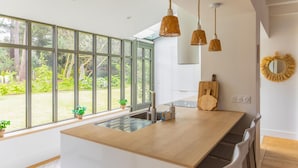 Een moderne keuken met grote ramen, een houten aanrecht en hangende pendelverlichting.