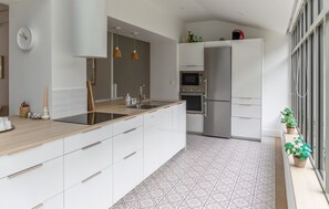 A modern kitchen with white cabinetry, a wooden countertop, a built-in oven, and a refrigerator. - Villa d'exception bord de mer (Noirmoutier en l'île)