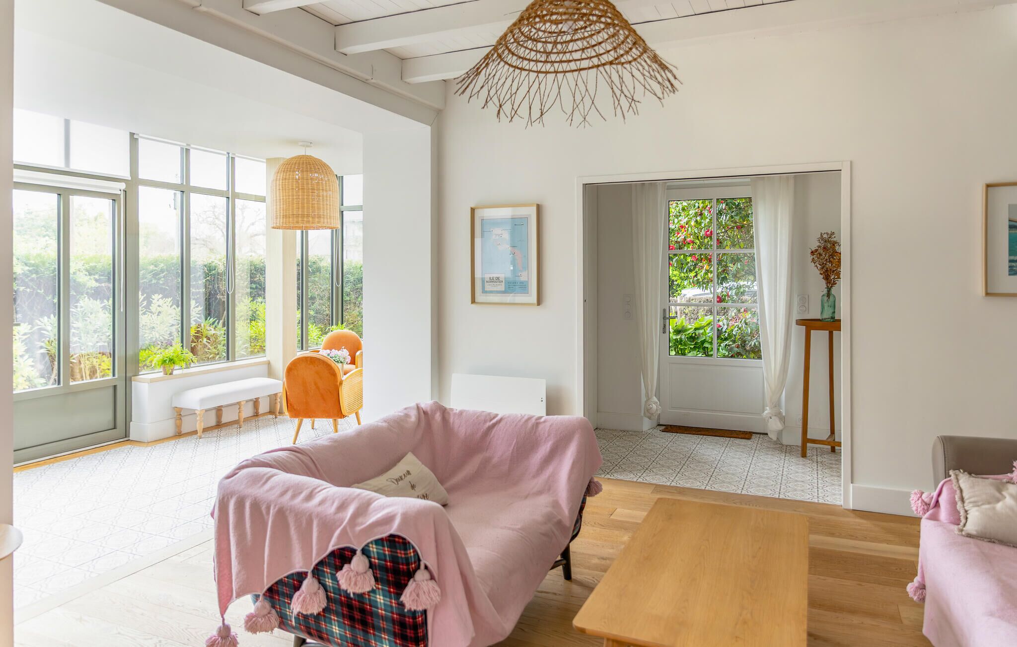Ein geräumiger Raum mit großen Fenstern, Holzboden, einem rosa Sofa, einem Holztisch und einer Korbtischlampe.