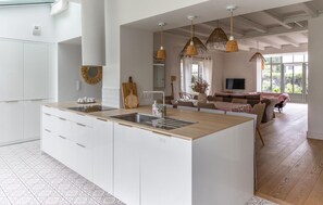 A modern kitchen with a central island, white cabinetry, and a dining area with a sofa and table. - Villa d'exception bord de mer (Noirmoutier en l'île)