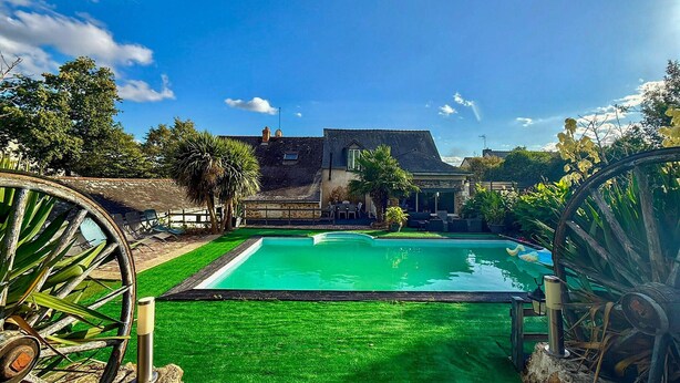 Una piscina con cubierta de madera, rodeada de césped cuidado y árboles.