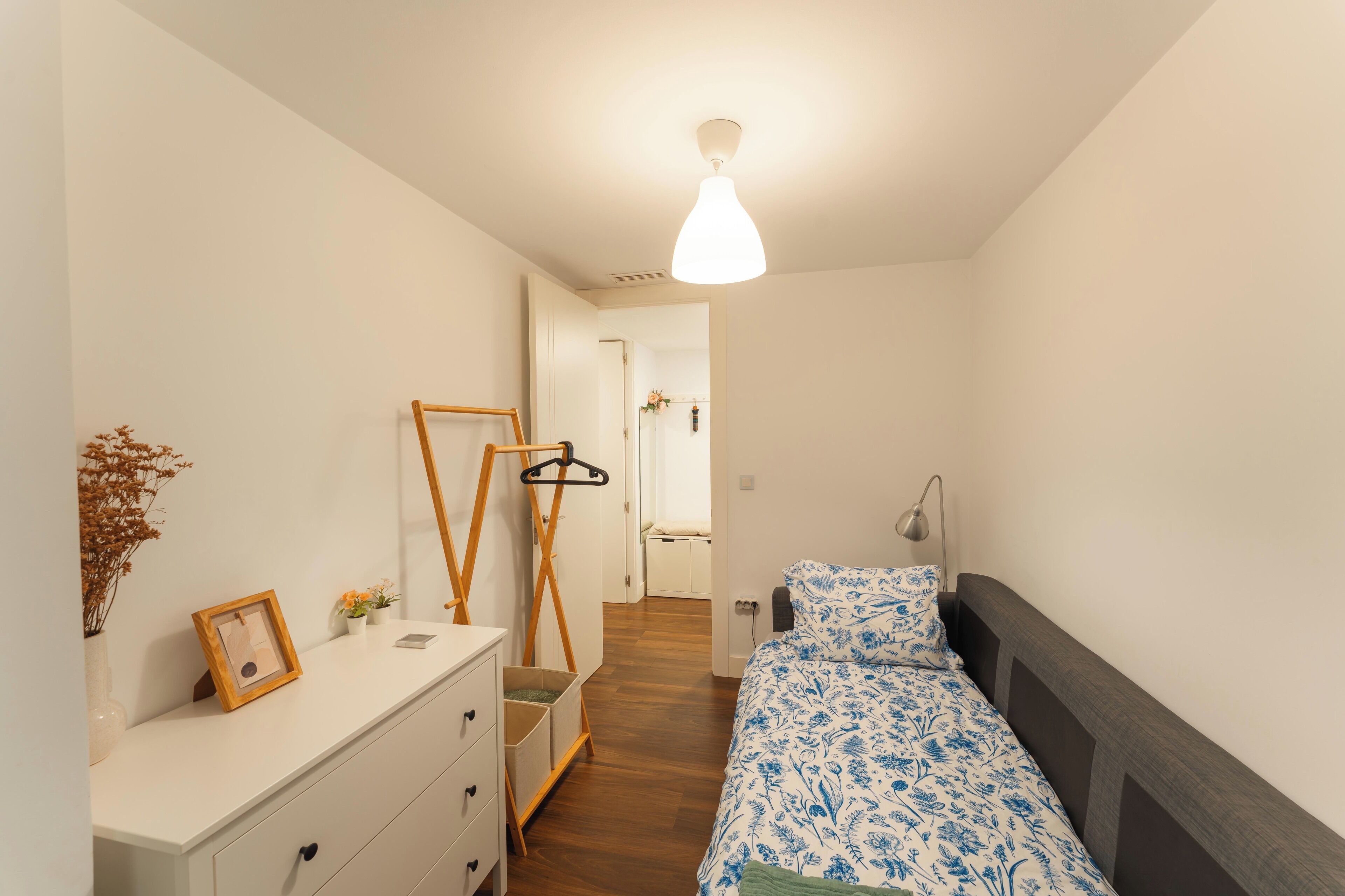Un dormitorio con cama, cómoda, espejo y perchero.
