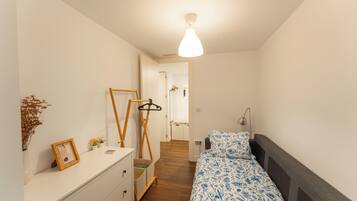 Un dormitorio con cama, cómoda, espejo y perchero.