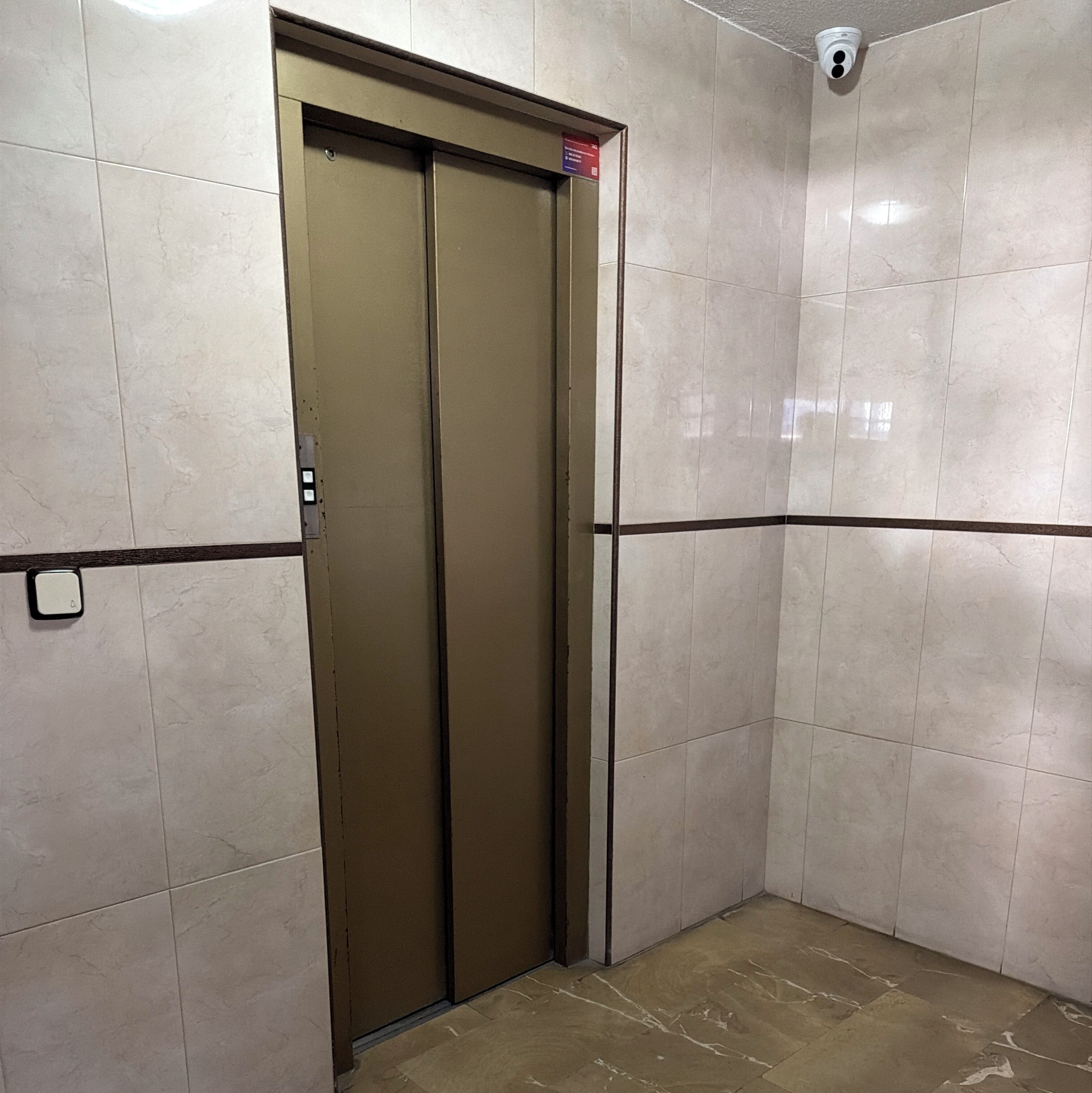 Un ascensore con porta chiusa, un pannello di controllo e una telecamera di sicurezza sopra.