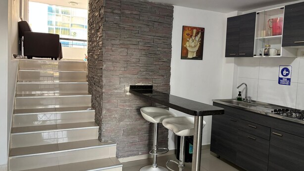Uma cozinha moderna com parede de detalhes em pedra, um banquinho de bar e uma escada que leva a uma área externa.