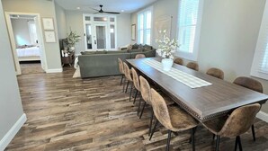 Un comedor espacioso con una larga mesa de madera y sillas modernas, una sala de estar acogedora con un sofá modular, y una cocina al fondo.