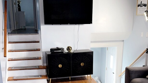 Una sala de estar moderna con una escalera, un televisor de pantalla plana, un mueble de entretenimiento negro y un sofá gris.