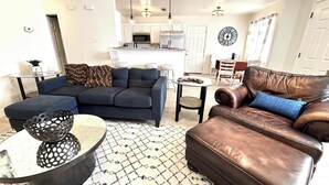 A modern living room with a dark blue sofa, a brown leather armchair, and a patterned rug. - Humble Haven - 2BR/1BA - Close to Hospitals (Lubbock)