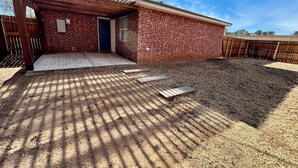 A single-story brick house with a covered porch, a fenced yard, and a clear sky. - Humble Haven - 2BR/1BA - Close to Hospitals (Lubbock)