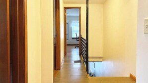 A hallway with wooden flooring and a black railing, leading to a room with a window. - Baseball Property 3 Separate Homes Sleeps 20. Multiple Families & Teams Welcome. (Oneonta)
