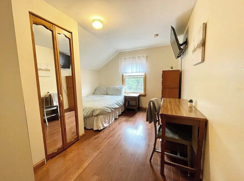 Ein kleines, gemütliches Zimmer mit einem Bett, einem Schreibtisch und einem Spiegel.