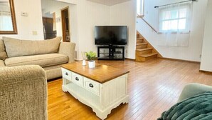 A living room with a wooden floor, a ceiling fan, a television, and a staircase. - Baseball Property 3 Separate Homes Sleeps 20. Multiple Families & Teams Welcome. (Oneonta)