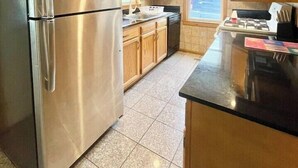 A modern kitchen with stainless steel appliances, wooden cabinets, and a large window providing natural light. - Baseball Property 3 Separate Homes Sleeps 20. Multiple Families & Teams Welcome. (Oneonta)