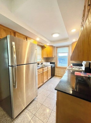 A modern kitchen with stainless steel appliances, wooden cabinets, and a large window providing natural light. - Baseball Property 3 Separate Homes Sleeps 20. Multiple Families & Teams Welcome. (Oneonta)