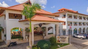 A multi-story building with a red-tiled roof, a covered entrance with palm trees, and a sign for 'Residencial Paraíso Restaurante La Bahia.' - Residencial Paraiso Bayahibe (Bayahíbe)