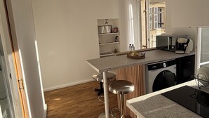 Ett modernt kök med en central köksö, barstolar, en tvättmaskin och en matplats med utsikt över omgivningen.