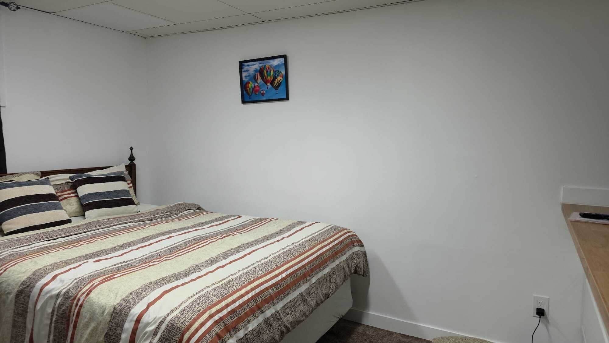A bedroom with a bed, a wooden headboard, a striped bedspread, and a painting on the wall.