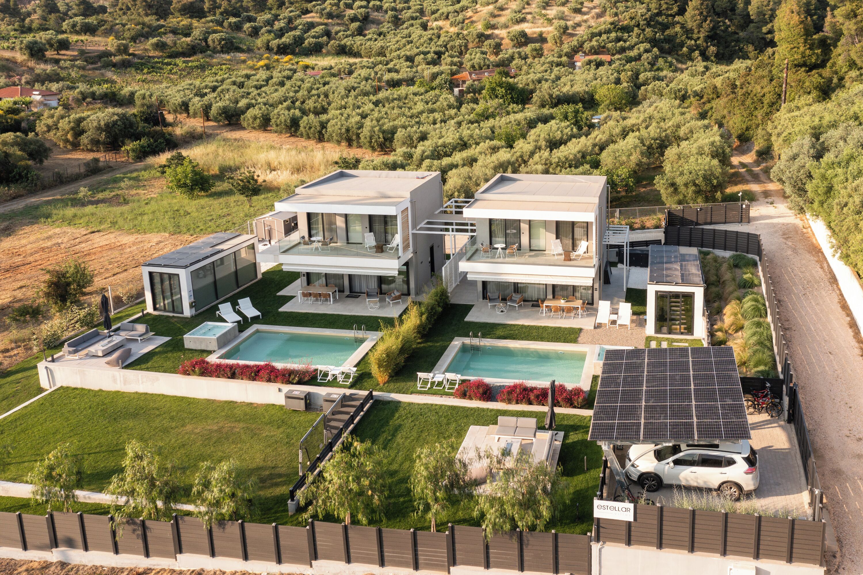 Une villa moderne dotée de deux piscines, de panneaux solaires et d’une voiture garée à l’extérieur.