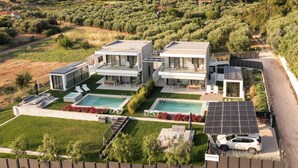 Una villa moderna con due piscine, pannelli solari e un'auto parcheggiata davanti.