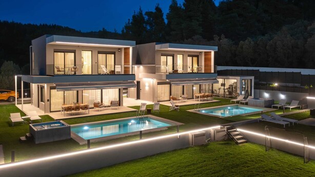 Una casa moderna de dos pisos con piscina, mobiliario exterior y un patio bien iluminado.