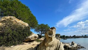 Una playa con aguas poco profundas y cristalinas, grandes formaciones rocosas y un árbol al fondo.