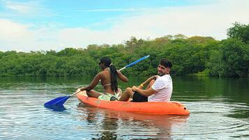 A group of people in a canoe on a calm river surrounded by dense greenery.